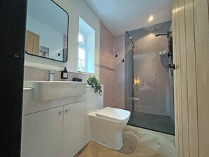 Un baño moderno con lavamanos, espejo y retrete blancos, cerramiento de ducha de vidrio y una planta en maceta sobre el mostrador.