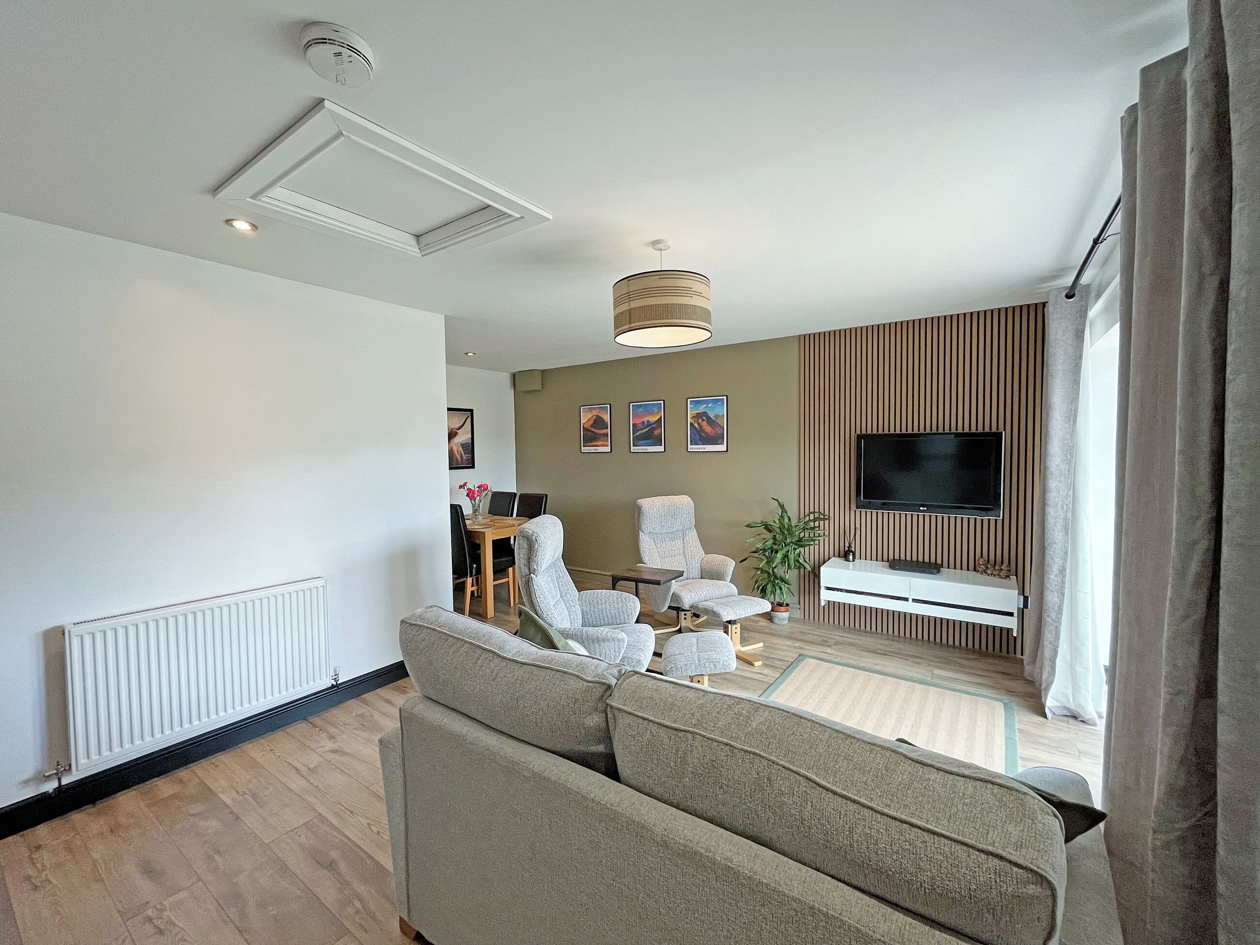 A modern living room with a sofa, armchairs, a TV, and a dining area.