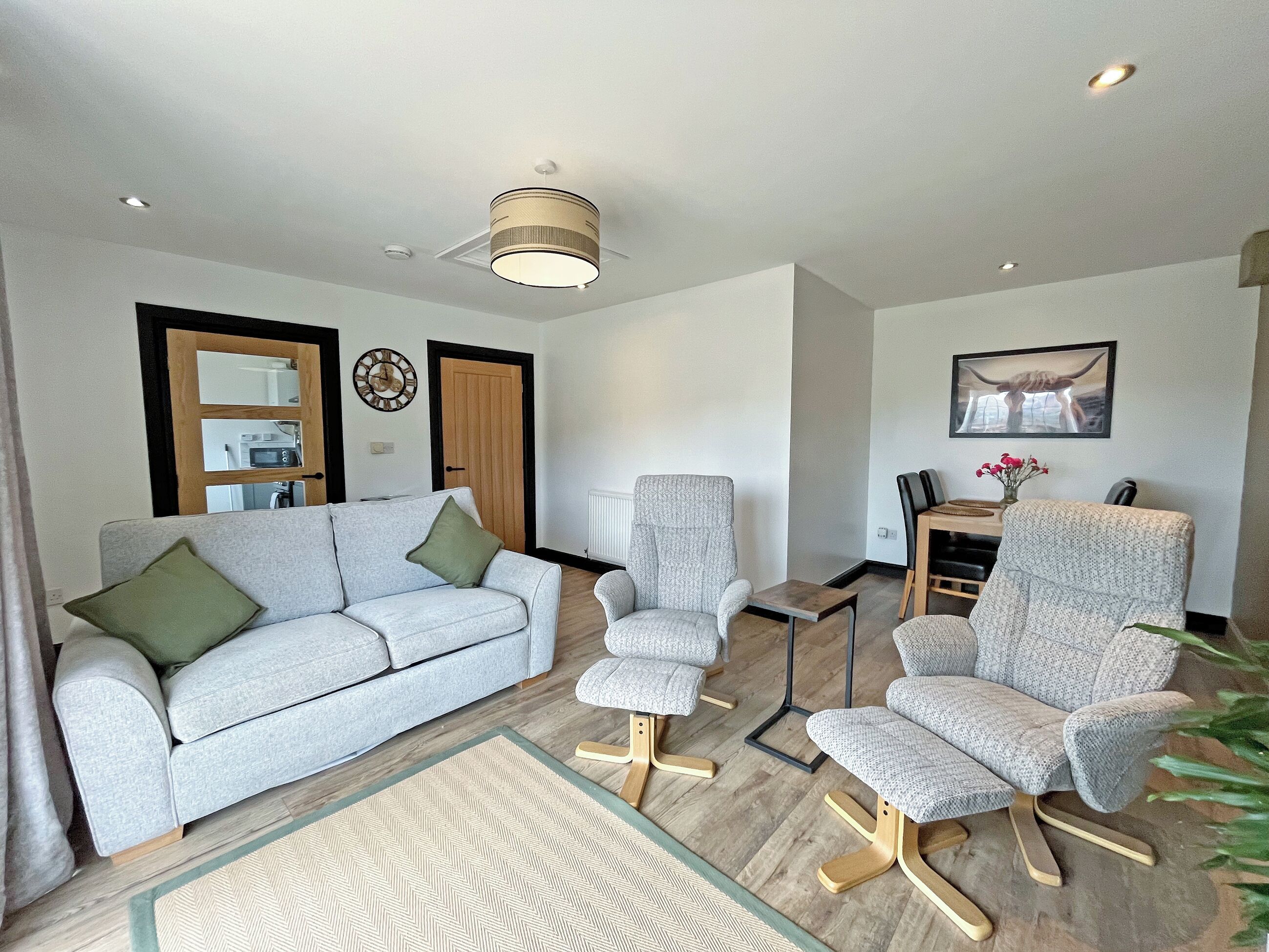 A living room with a sofa, two armchairs, a coffee table, a wall-mounted clock, and a framed picture.