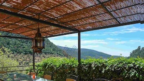 Un tavolo da pranzo con piano in vetro, sedie, una lanterna sospesa e vista su un paesaggio montuoso.