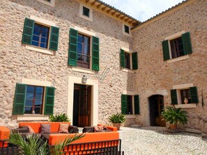 Un patio con muros de piedra, contraventanas verdes, mobiliario exterior y plantas en macetas.