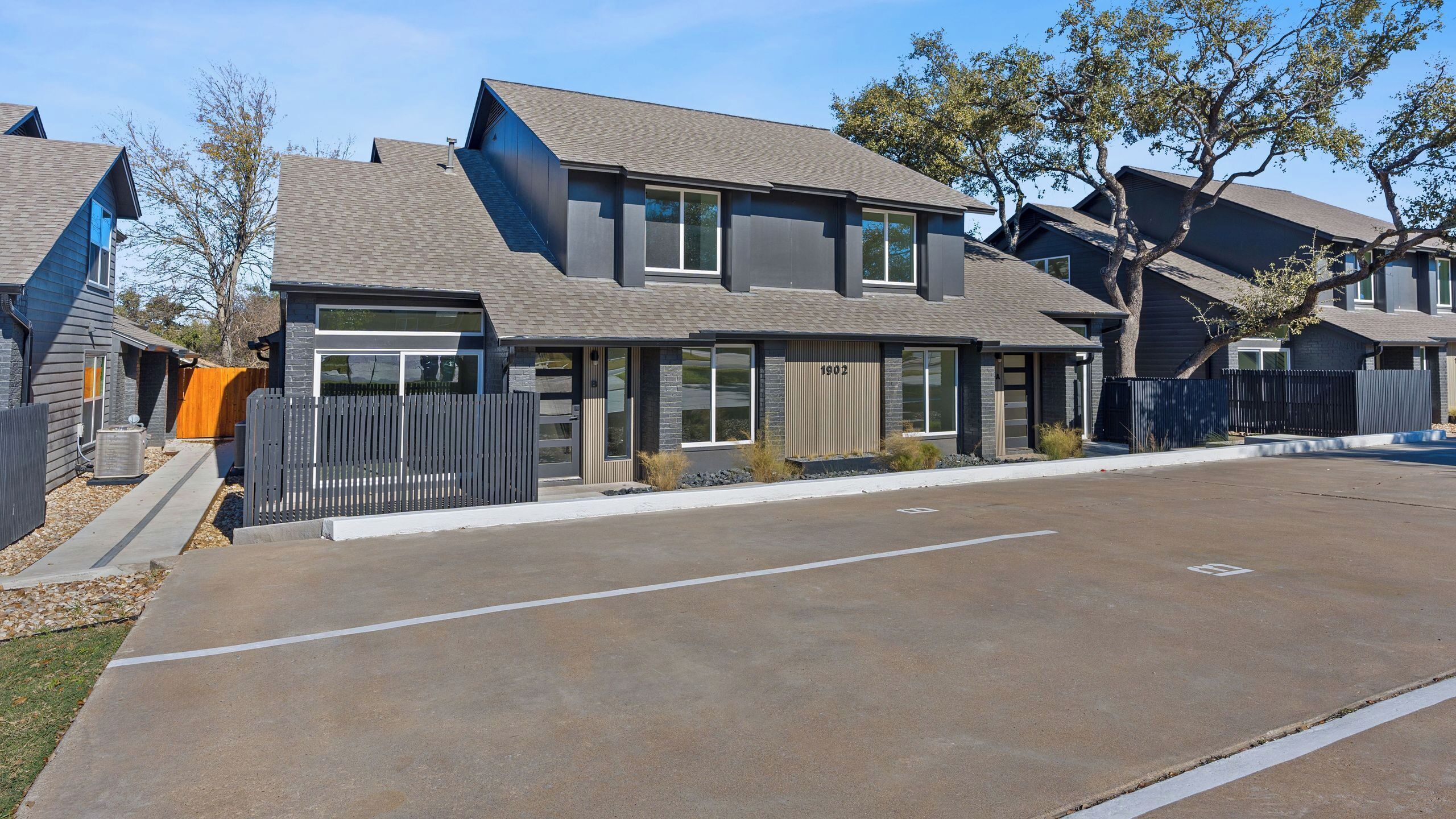A modern two-story residential building with a garage, a fenced yard, and a clear driveway.