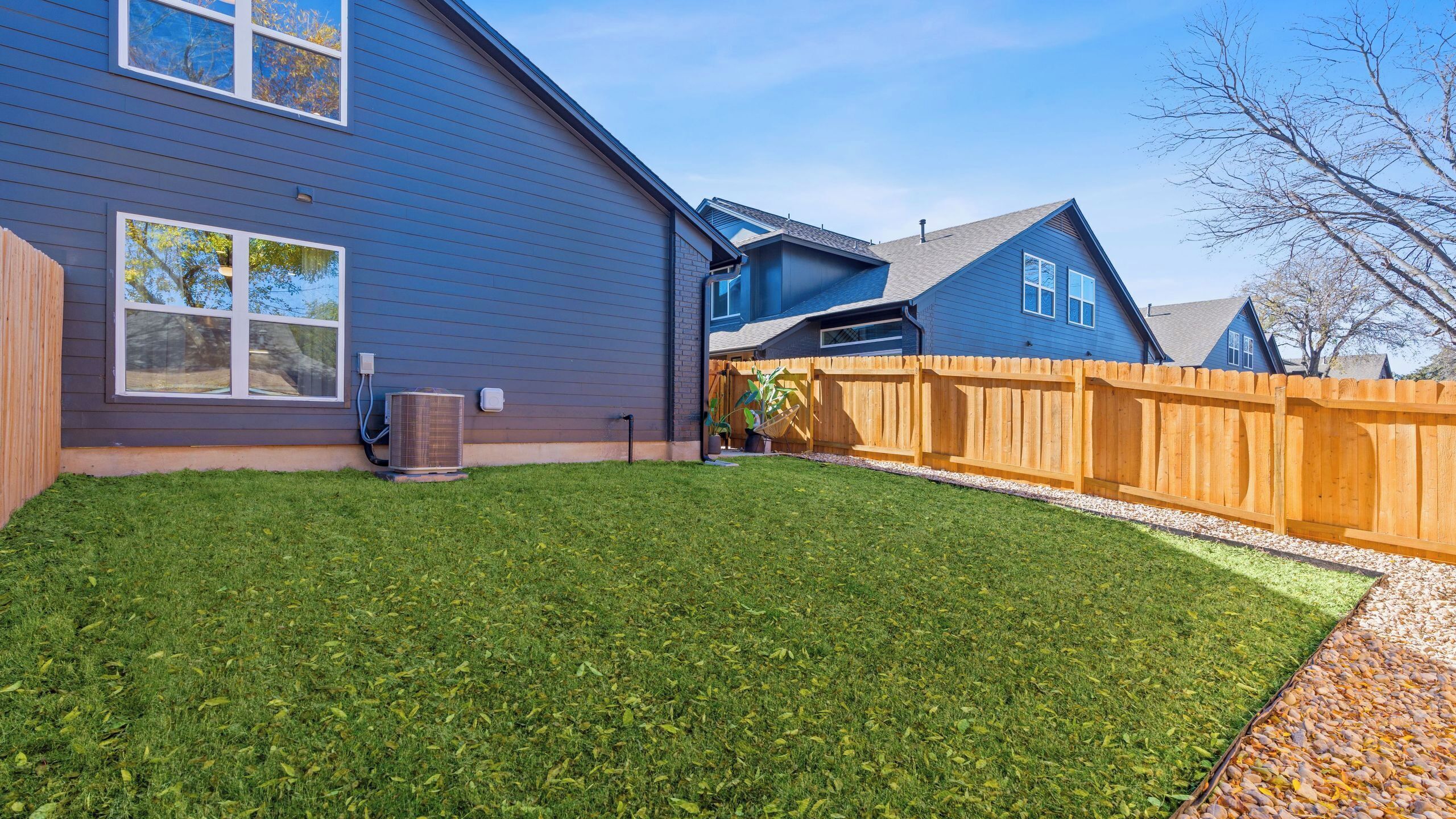 A residential property with a well-maintained lawn, a wooden fence, and a clear sky.