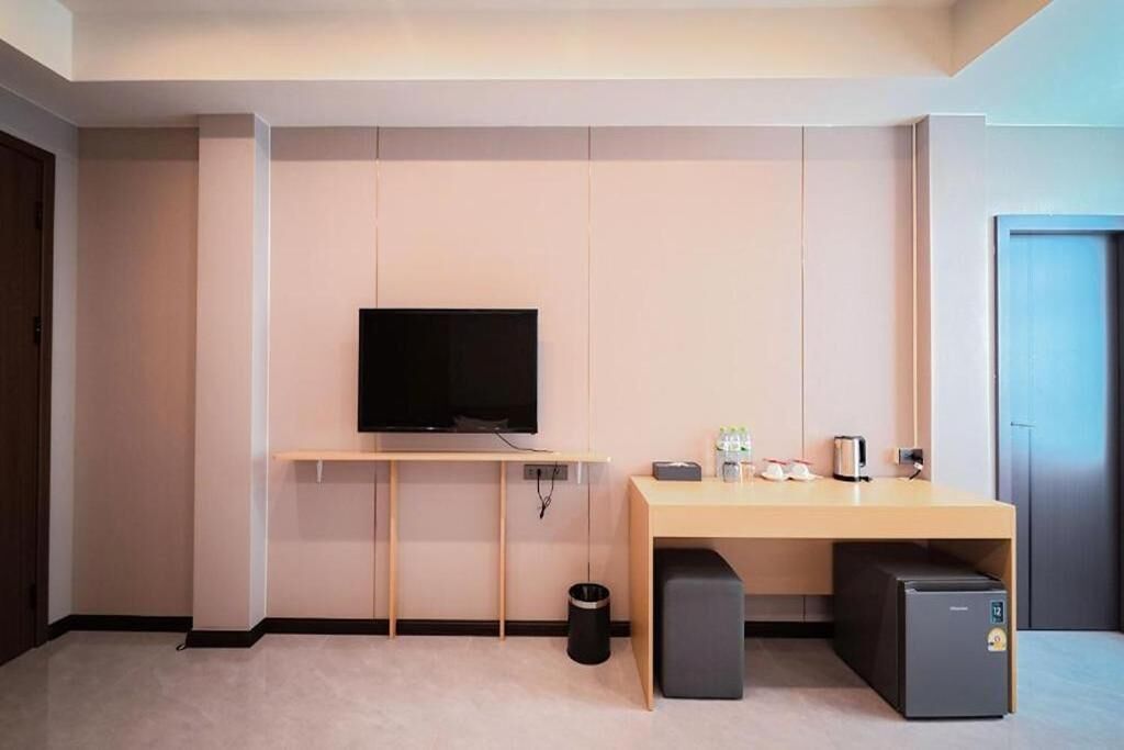 A modern room with a flat-screen TV mounted on a wall, a wooden desk with a small refrigerator, and a trash can.