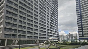 A modern high-rise building with a grid of balconies, a metal sculpture in the foreground, and a clear sky.