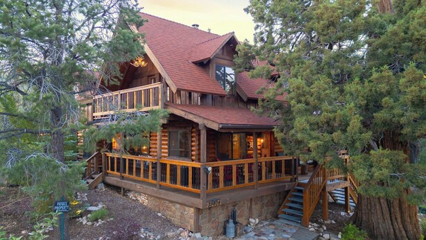 A log cabin with a balcony, stone foundation, and a staircase leading to the entrance.