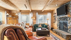 A log cabin interior with a fireplace, leather furniture, and a television.