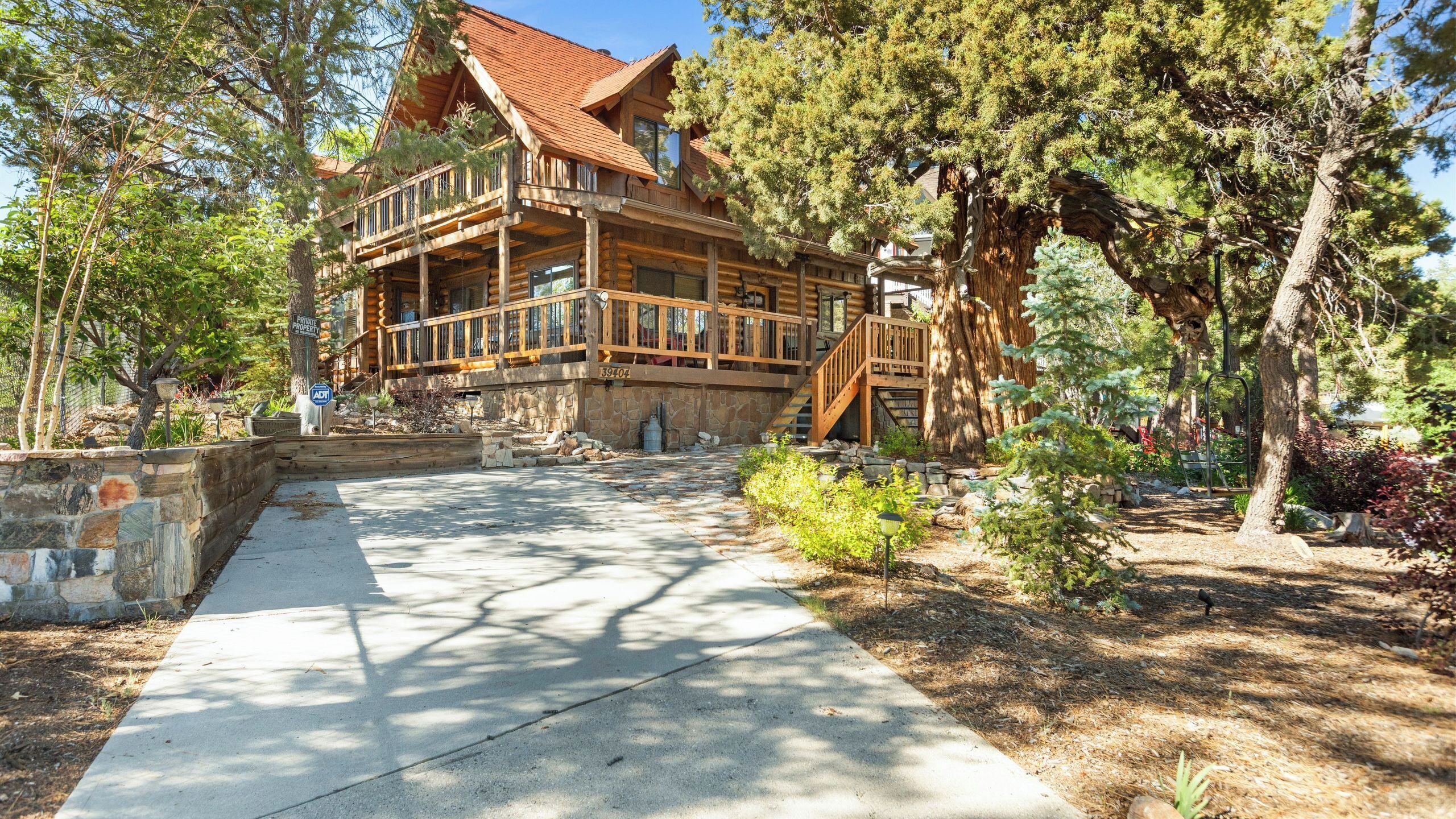 A log cabin with a stone foundation, wooden deck, and a staircase leading to a balcony.