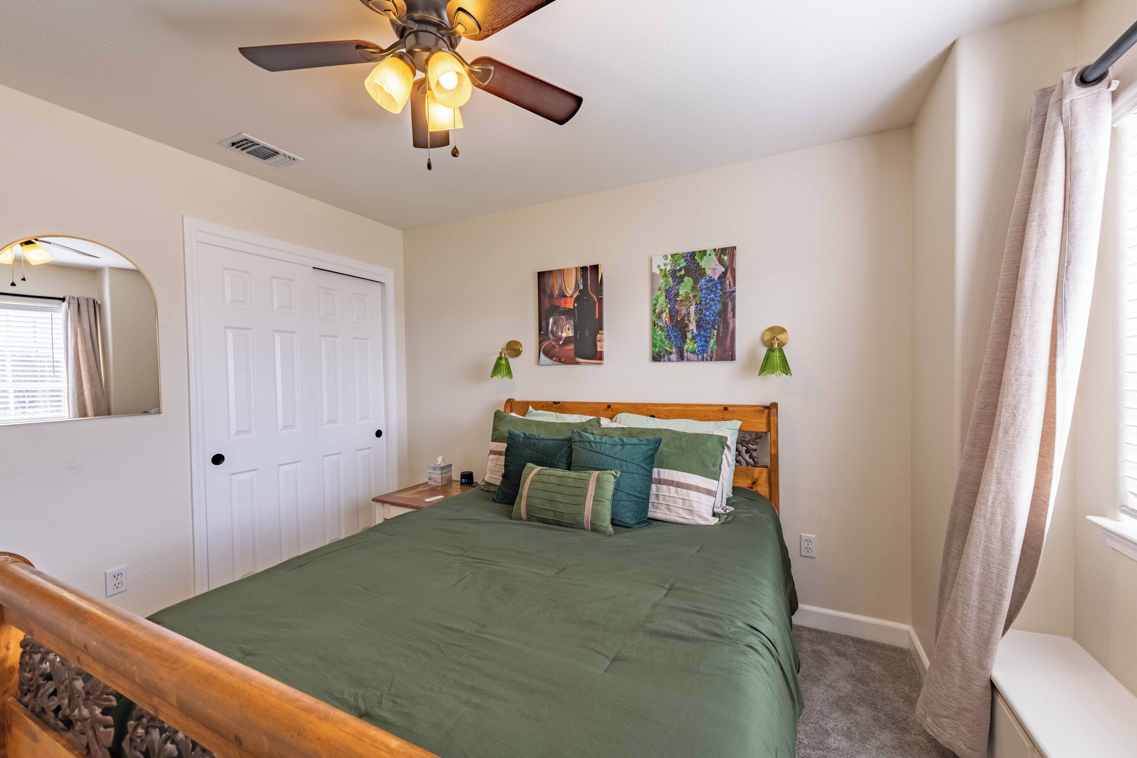 A bedroom with a bed, a ceiling fan, a door, and wall art.