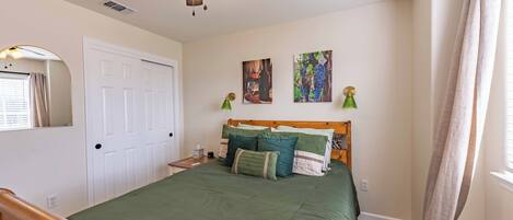 A bedroom with a bed, a ceiling fan, a door, and wall art.
