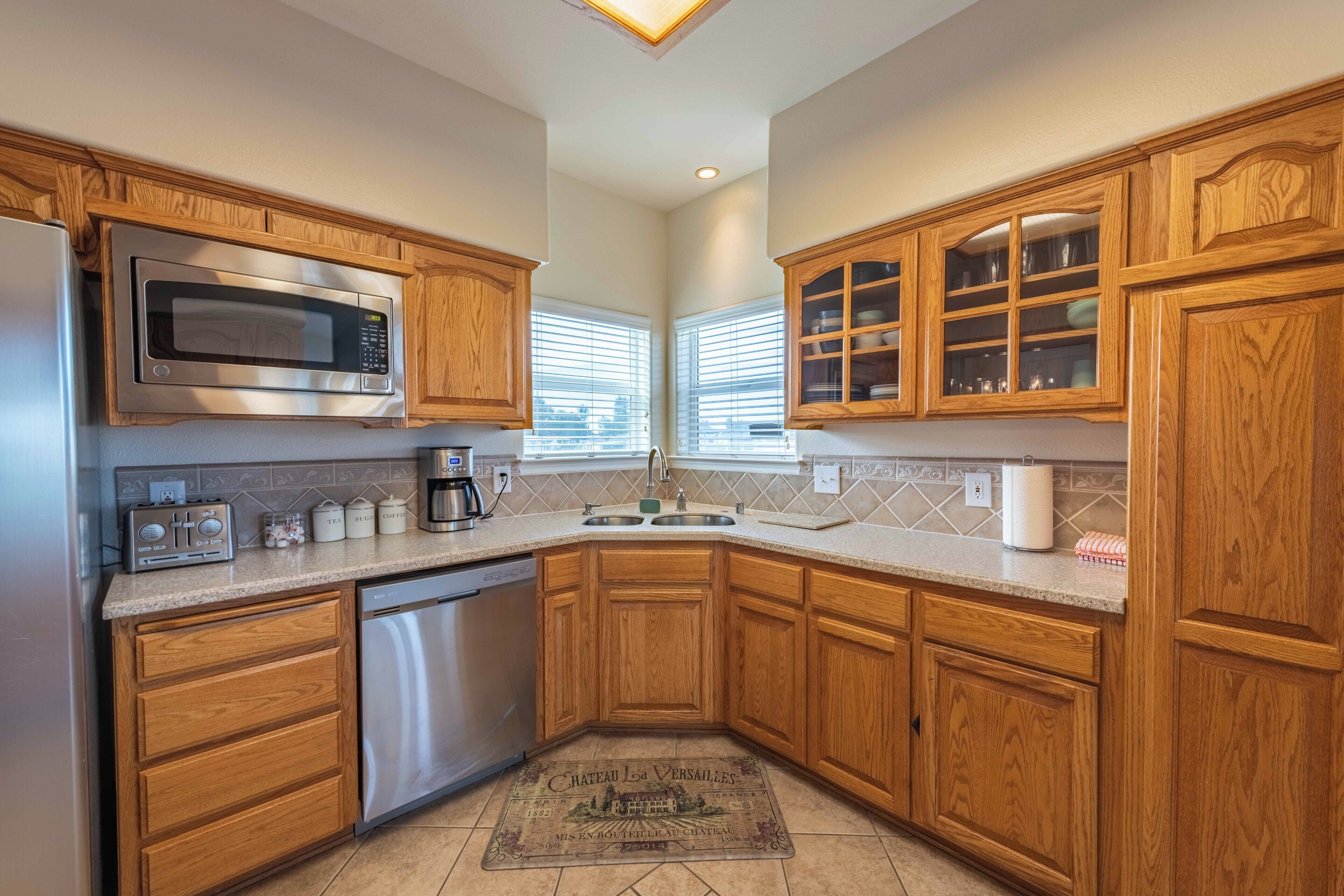 A kitchen with wooden cabinets, a microwave, a dishwasher, and a window with blinds.