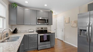 A modern kitchen with grey cabinets, a stainless steel refrigerator, a built-in microwave, a stove, and a sink. - Red Bud Sycamore by Avantstay Custom Group Retreat w/ Patio (Asheville)