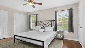 A bedroom with a bed, a ceiling fan, two windows with curtains, and a door. - Red Bud Sycamore by Avantstay Custom Group Retreat w/ Patio (Asheville)