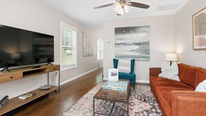 A living room with a flat-screen TV, a wooden coffee table, a patterned rug, a teal armchair, and a brown sofa. - Red Bud Sycamore by Avantstay Custom Group Retreat w/ Patio (Asheville)
