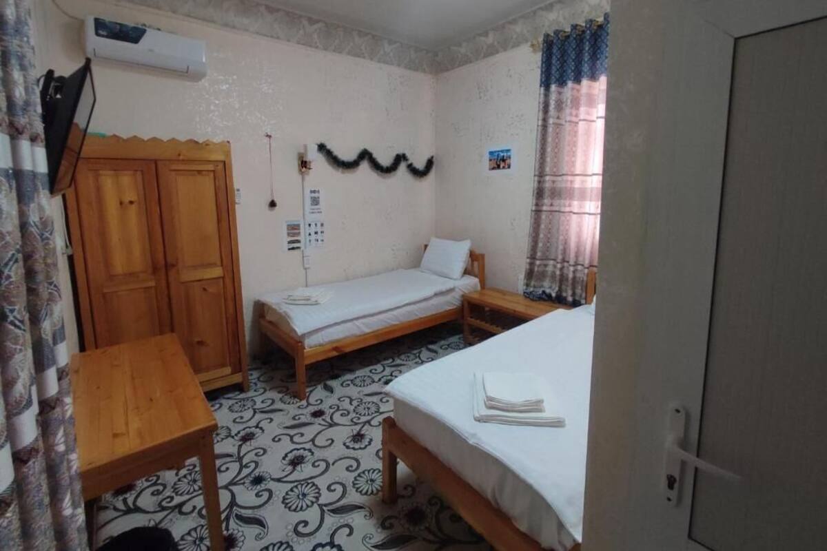 Una habitación con dos camas, una mesa de madera, un armario, un equipo de aire acondicionado y un calendario en la pared.