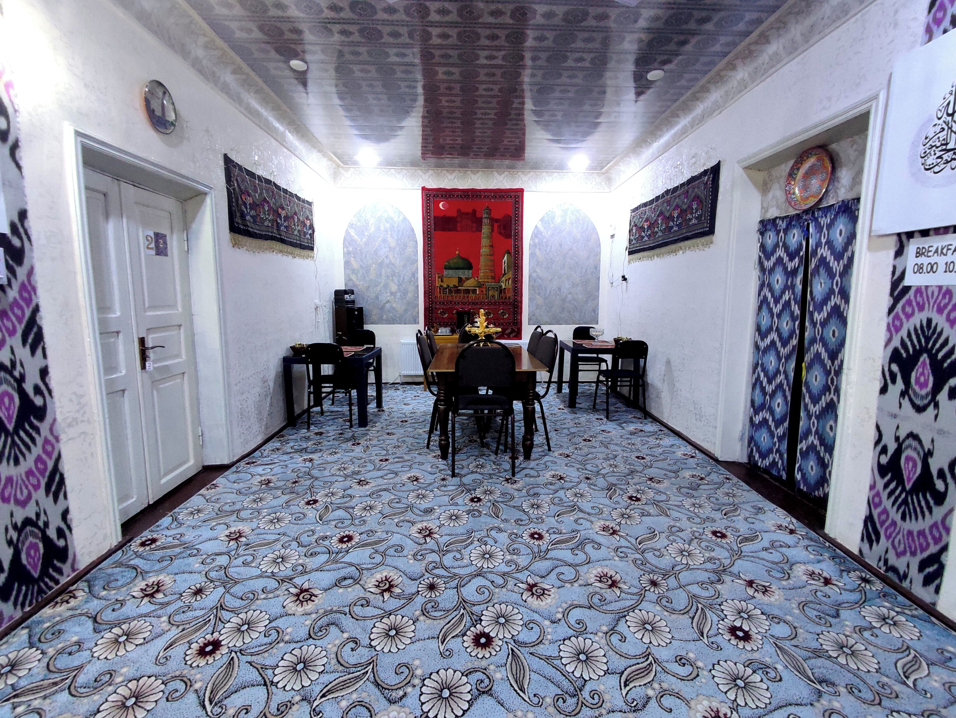 Um corredor com piso estampado, uma área de refeições com cadeiras e uma mesa, e uma porta à esquerda.