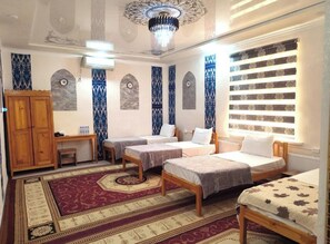 A room with three beds, a wooden wardrobe, a desk, and a patterned carpet. - oybek hotel (Khiva)