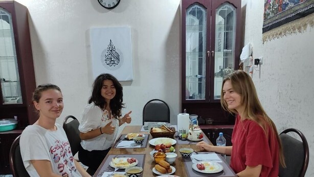 A dining table with food, a clock, and a cabinet in a room. - oybek hotel (Khiva)