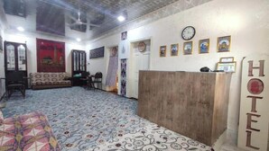 A hotel reception area with a wooden desk, a clock, and framed pictures on the wall. - oybek hotel (Khiva)