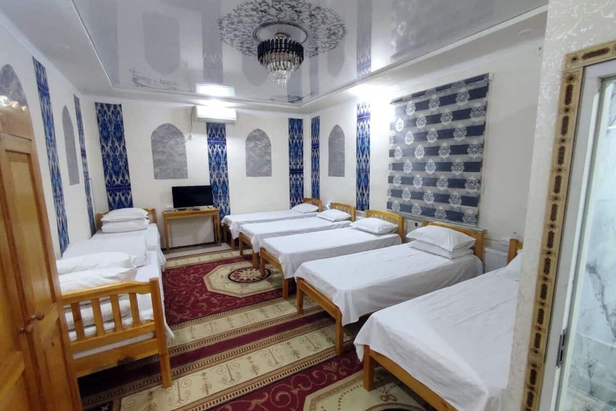 Habitación de hotel con cuatro camas individuales, una silla de madera, un televisor y paredes con diseño.