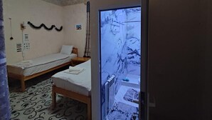 A room with two beds, a radiator, and a television displaying a snowy scene. - oybek hotel (Khiva)