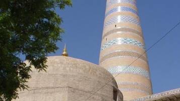 A tall, cylindrical tower with a dome and patterned design, surrounded by a building with a flat roof and a balcony.