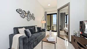 Ein modernes Wohnzimmer mit grauem Sofa, Couchtisch, Fernseher und Balkon mit Blick.