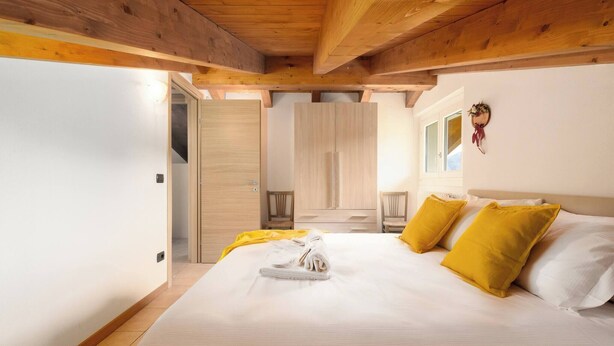 Ein Schlafzimmer mit Holzbalkendecke, einem Bett mit weißen und gelben Kissen und einem ordentlich bezogenen Bett.