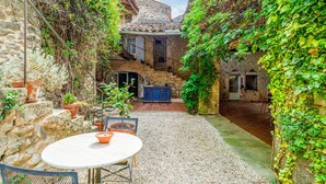 A courtyard with a stone wall, a table with chairs, and a blue cabinet. - 2-person gîte with Gardoise vault in a restored 16th-century mas, 15 km from Uzès (Lussan)