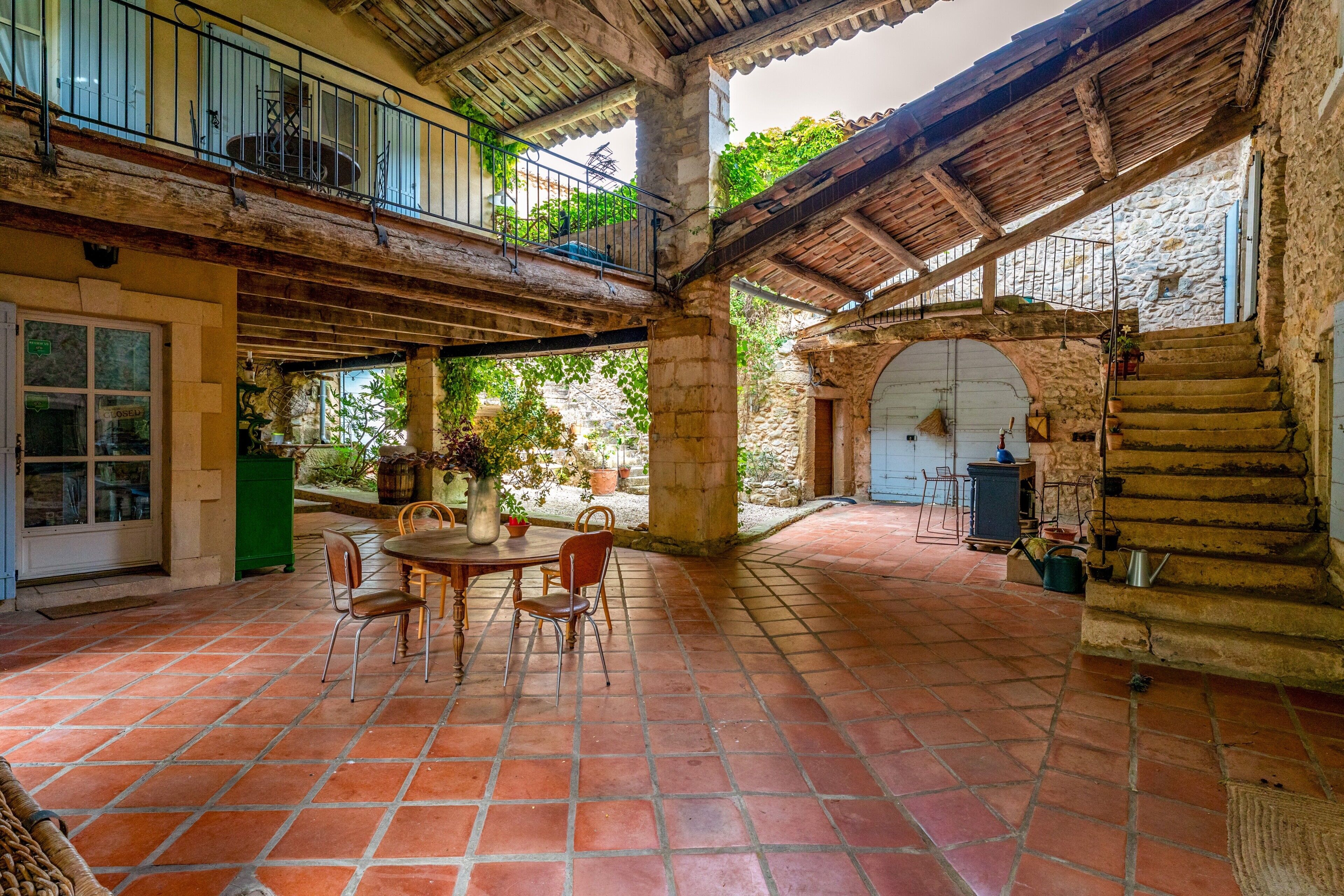 A courtyard with a table and chairs, stone walls, and a wooden balcony.