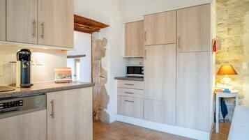 Une cuisine avec des meubles de couleur bois clair, une machine à café, un four à micro-ondes et une petite table avec une lampe.