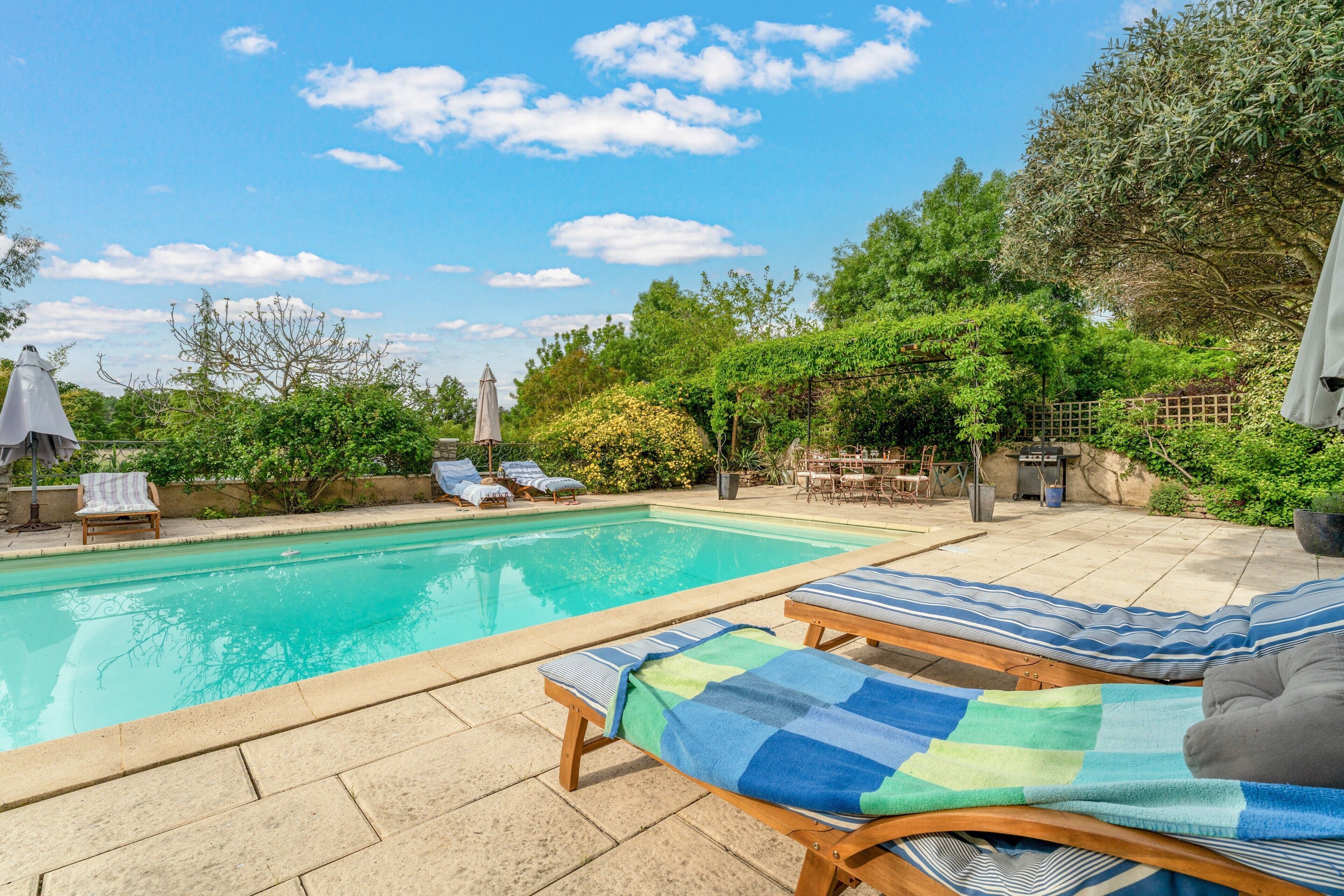 Une piscine avec des chaises longues, un espace patio et une végétation luxuriante tout autour.