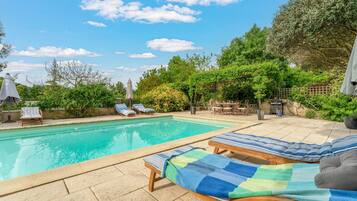 Une piscine avec des chaises longues, un espace patio et une végétation luxuriante tout autour.