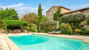 A swimming pool with lounge chairs, a stone building, and surrounding greenery.