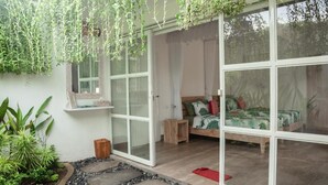 A room with a bed, a small wooden stool, and a window with a view of the outside. - Tulus Hati Ubud Retreat (Ubud)