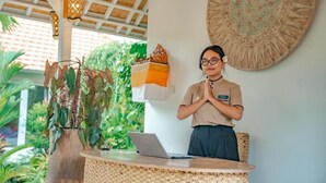 A reception desk with a laptop, a woven chair, a decorative wall piece, and a potted plant. - Tulus Hati Ubud Retreat (Ubud)