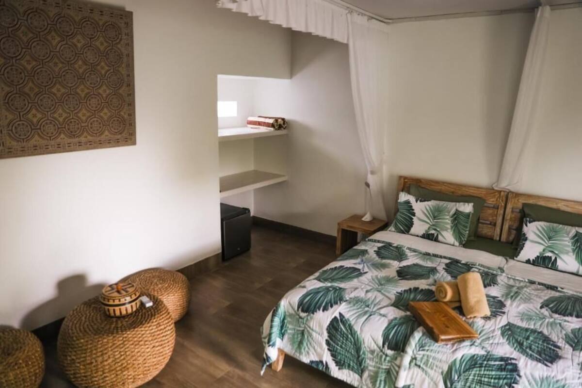 A bedroom with a bed, bedside tables, a nightstand, a wall-mounted shelf, and a decorative wall panel.