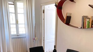 Un coin repas avec une table blanche, des chaises noires et un élément décoratif rouge sur le mur.