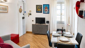 Un salon moderne avec un canapé gris, une table à manger dressée pour quatre personnes, un téléviseur posé sur un meuble et des œuvres d’art accrochées aux murs.