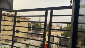 A balcony with a metal railing, a tiled floor, and a view of neighboring buildings. - Citistay Apartments (Abuja)