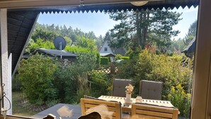 Een raam met uitzicht op een tuin, een houten tafel met stoelen, en decoratieve visbeeldjes.