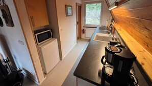 Een kleine keuken met een magnetron, koelkast, spoelbak en koffiezetapparaat.