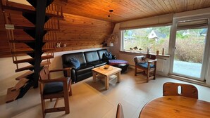 Een gezellige kamer met een houten trap, een zwarte leren bank, houten stoelen, een kleine tafel en een raam met uitzicht.