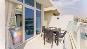 Ein Balkon mit Tisch, Stühlen, einer Couch und einer Glastür zu einem Raum mit Bett und Vorhängen.