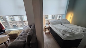 Quarto moderno com cama, sofá, mesa pequena e janela com vista para edifícios.