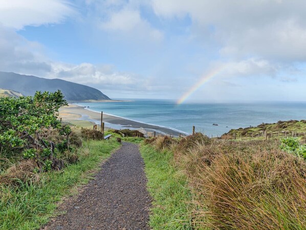 A coastal path leading to a beach with a mountain in the background and a rainbow.