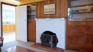 A room with a fireplace, wooden cabinets, a table, and a window.