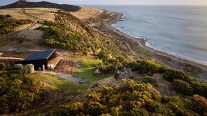 A coastal landscape with a building featuring a sloped roof, situated on a hillside overlooking the beach.