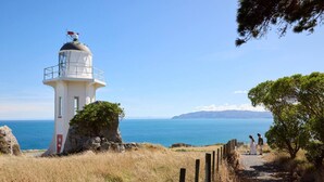 A lighthouse on a cliff overlooking a coastal area with a clear sky.