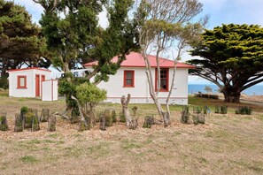A white building with red trim and a red roof, surrounded by trees and a fence.